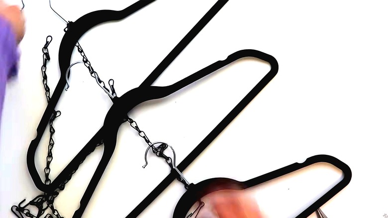 Person assembling a vertical clothes hanging solution by connecting three hangers with a chain