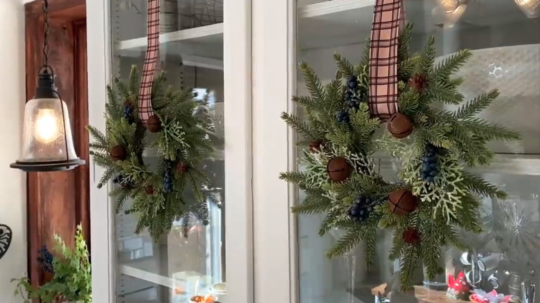 Mixed greenery wreaths with rusty bells and plaid ribbon