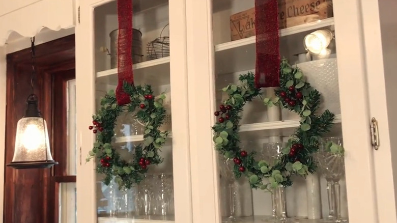 Wreaths featuring eucalyptus and red berries on glass cabinets
