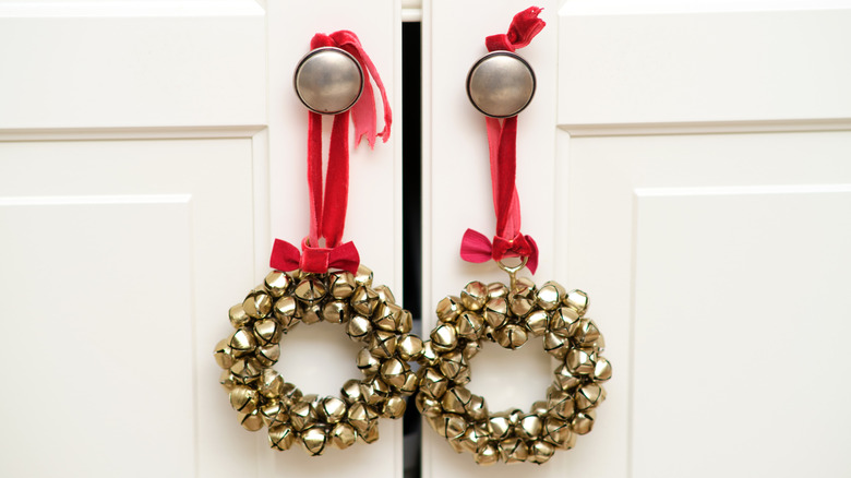 Golden jingle bell wreaths with red ribbons hanging on white cabinet knobs
