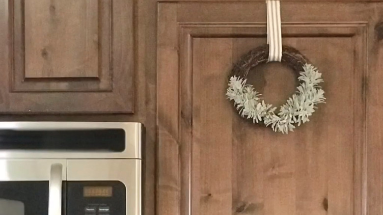 Rustic rattan wreath with white frosted leaves on wood cabinet