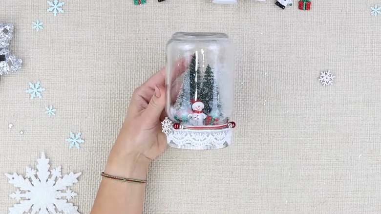 Someone's hand holding a decorated snow globe in a jar