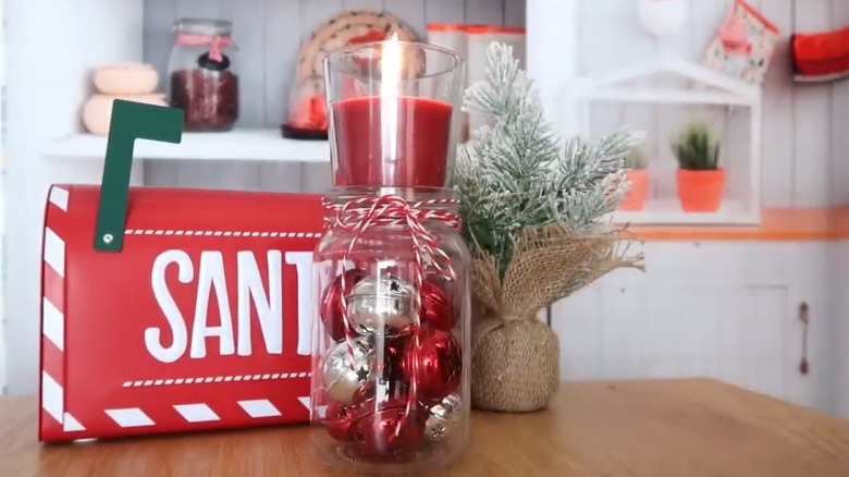 Red and silver Christmas ornaments in a glass jar beneath a lit red votive candle