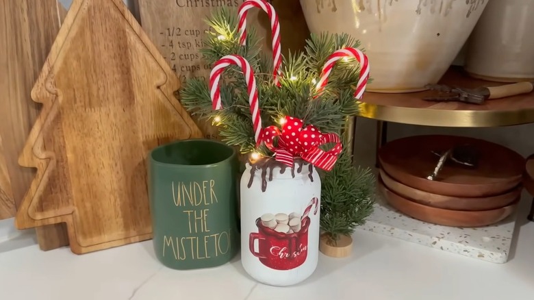 A white painted mason jar holding winter foliage, candy canes, and fairy lights