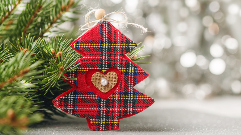 A tartan Christmas tree decoration next to a Christmas tree branch on a sparkly white background