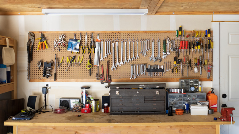 Workbench area in a garage with tools hung on pegboard above workbench