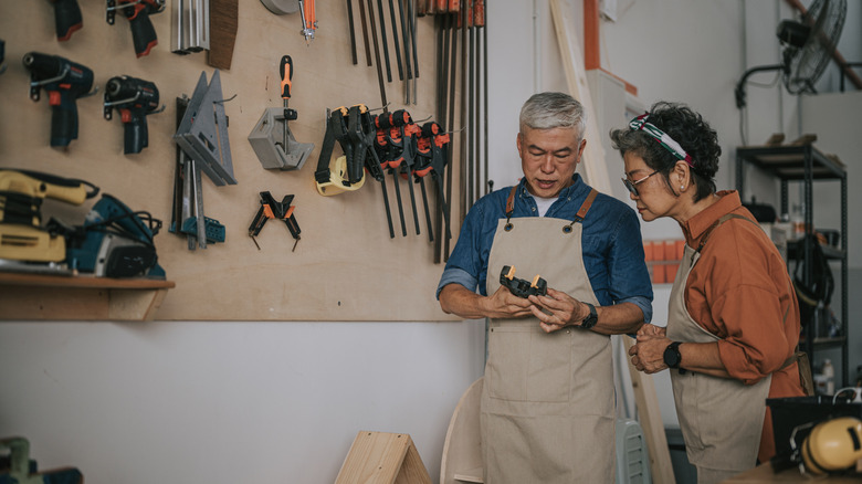middle-aged couple going through their tools in front of a large pegboard