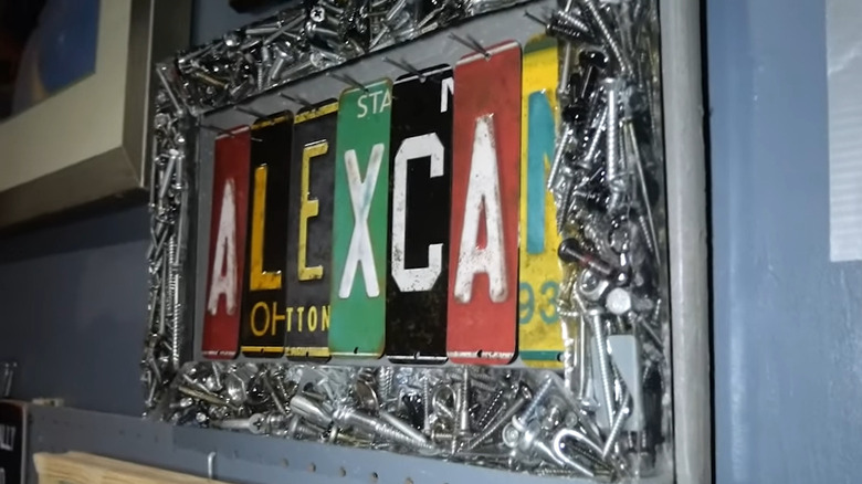 Picture frame made of resin filled with nuts and bolts along with screws framing slices of a license plate spelling ALEX CAN