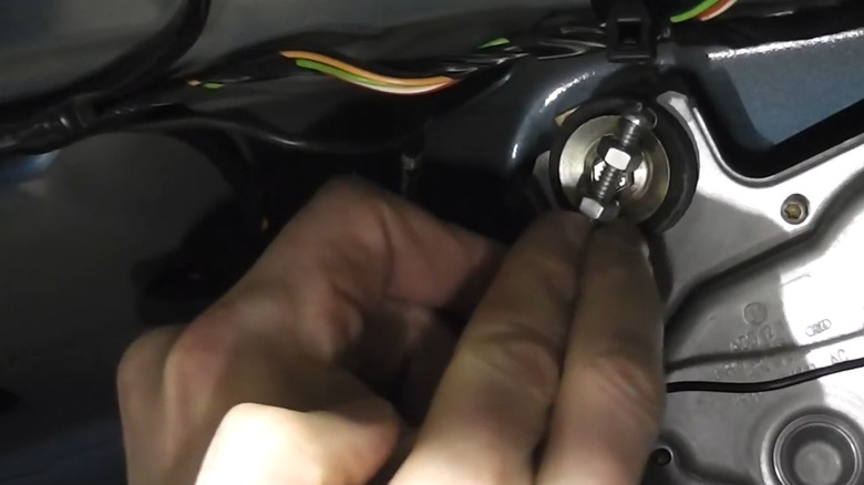 Hand using a DIY wrench made of nuts and bolts in a car trunk