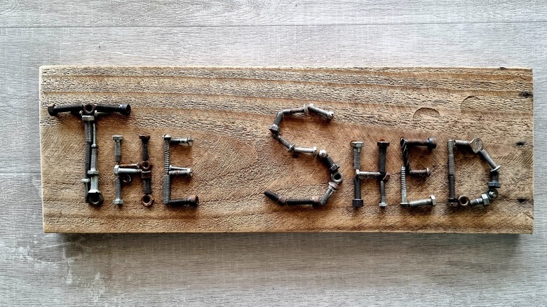 Screws, nuts, and bolts spelling out the words THE SHED on a piece of wood