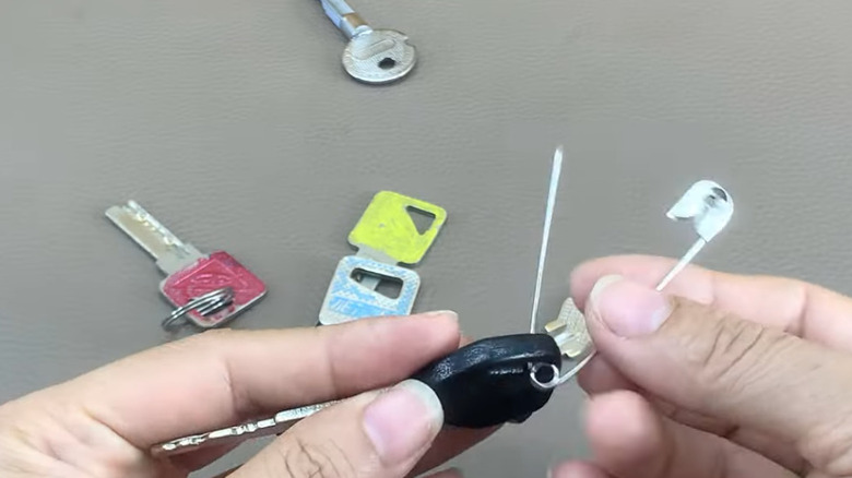 Someone putting car and house keys on large safety pin