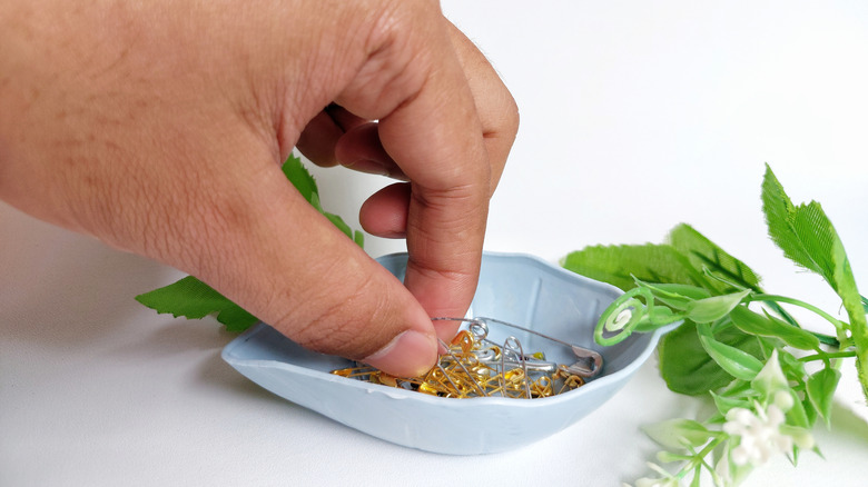 Hand digging into light blue bowl with silver and gold safety pins