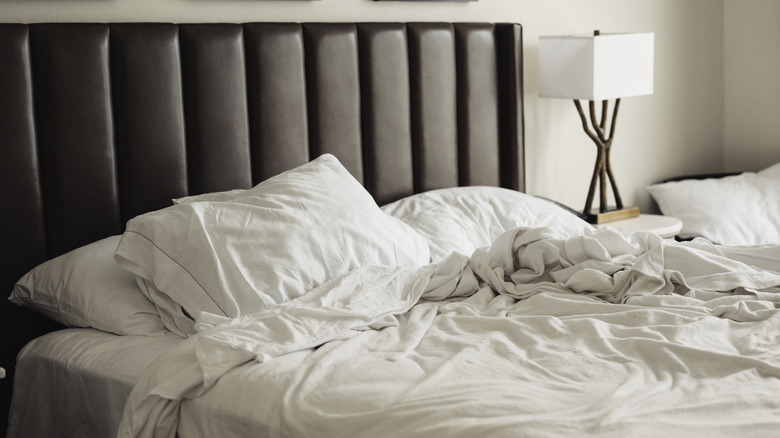 Messy bedding on a bed with a brown padded headboard