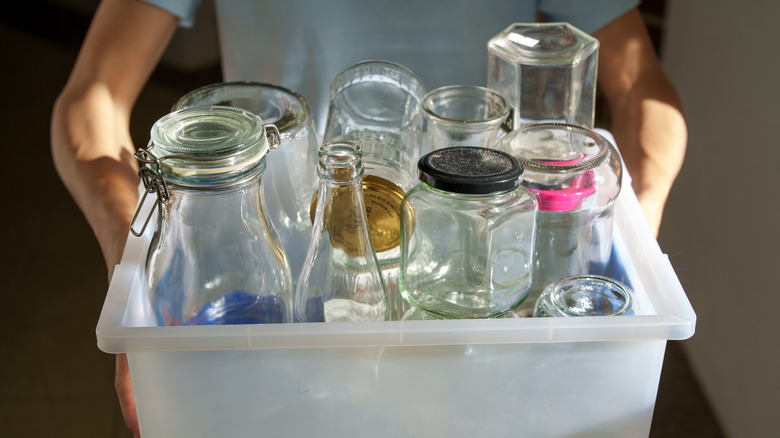 A person holds a plastic tub full of old glass jars and bottles.