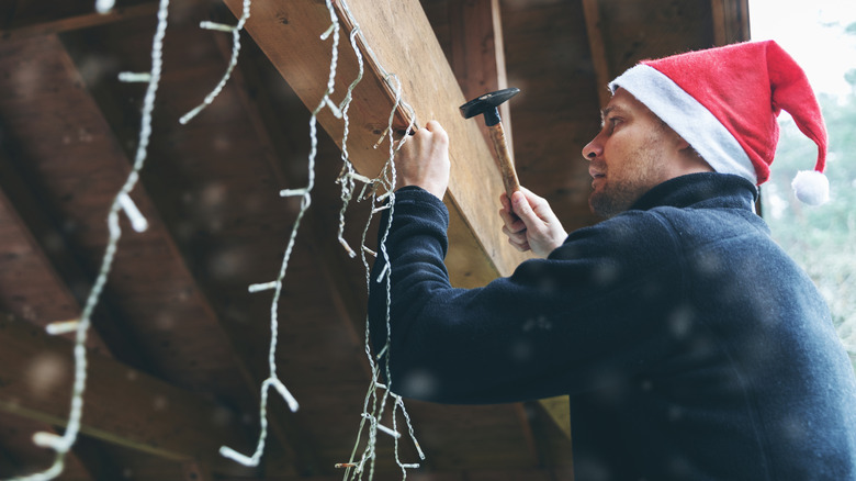man with santa hat decorating house outdoors