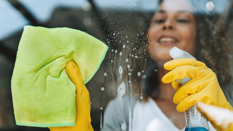 Smiling woman spraying glass cleaner on a window