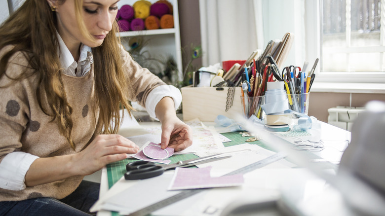 A woman crafting on a disorganized desk.