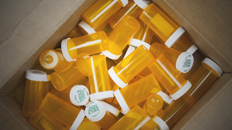A cardboard box full of empty yellow pill bottles.