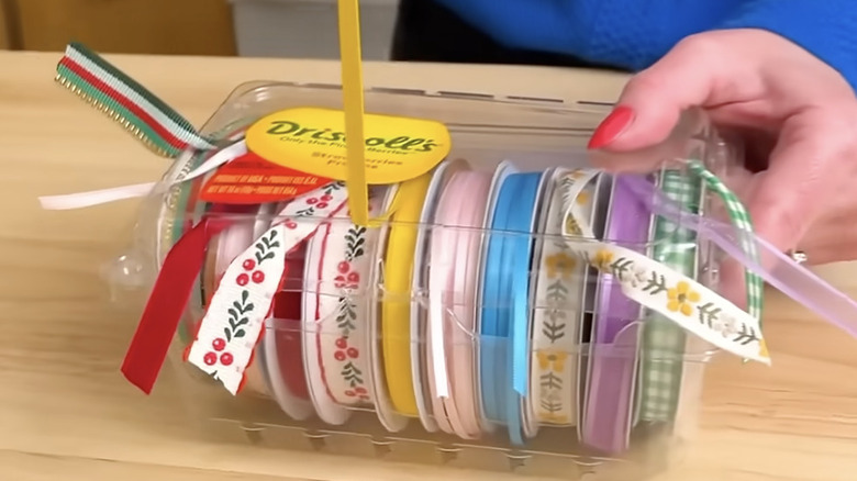 Rolls of ribbon stored in a repurposed plastic fruit container.