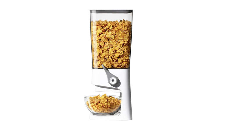 The OXO food dispenser with cereal inside and a bowl below the dispenser on a white background