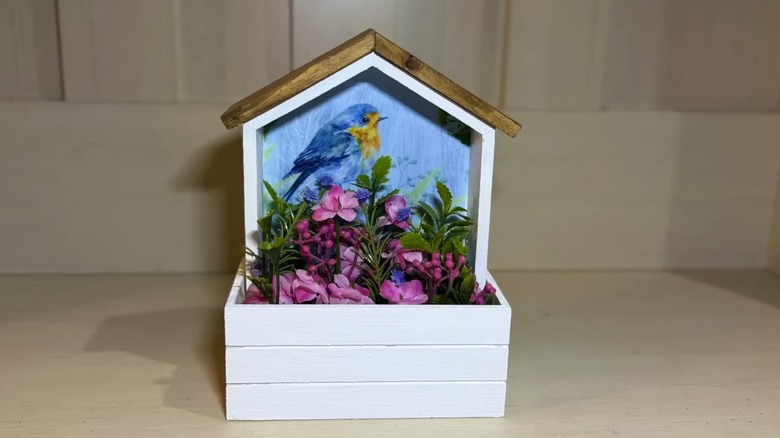 A small white bird house filled with flowers