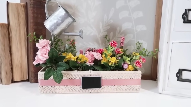 A beautiful flower-filled plant stand with a watering can on top