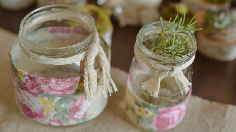 Two small jars with fabric sleeves and one with a rosemary sprig in it