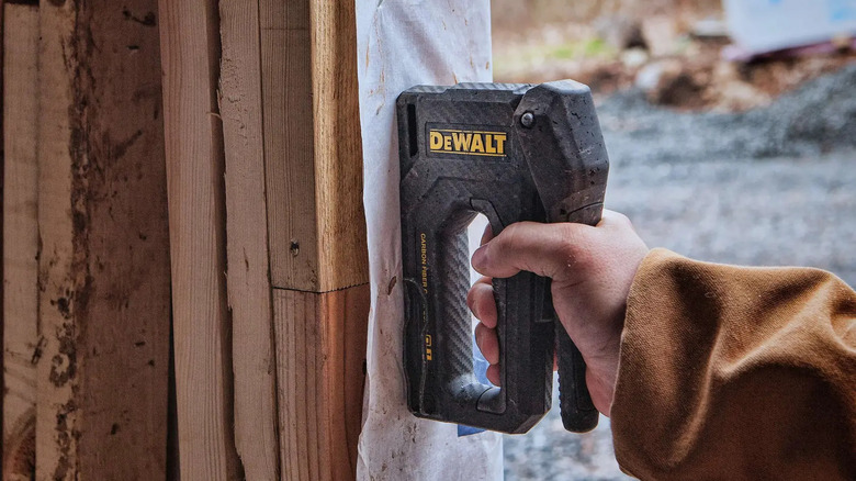 A person using DeWalt's Carbon Fiber Stapler/Tacker to fix fabric to a fence