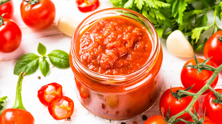 Salsa jar with paste in it and tomato surrounding it