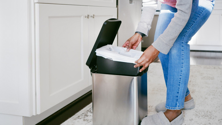 Woman putting trash bag into kitchen trash can