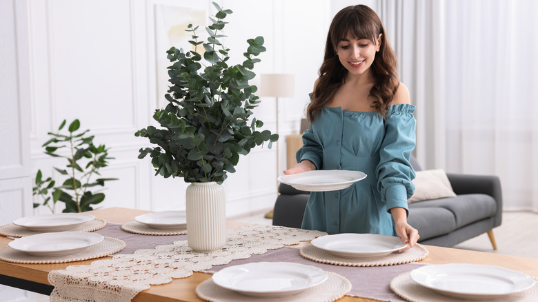 A person setting the table with white plates