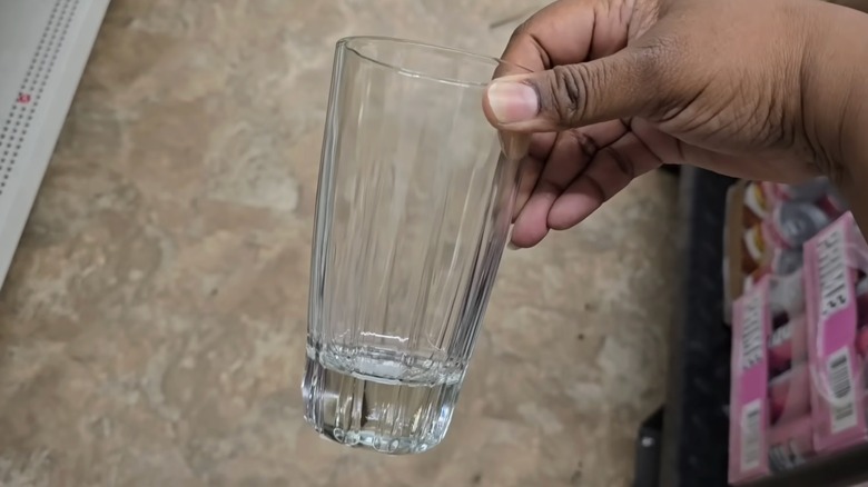 Person's hand holding up a clear glass Dollar Tree drinking cup that looks like it could be made of crystal.