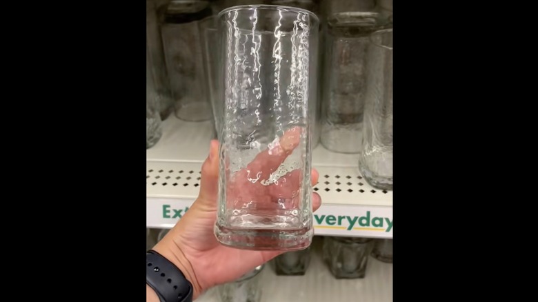 Screenshot of TikTok video, showing a person's hand holding a textured glass cup by a store shelf.