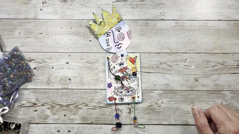 Character made out of a joker card, wire, and beads on a wood background