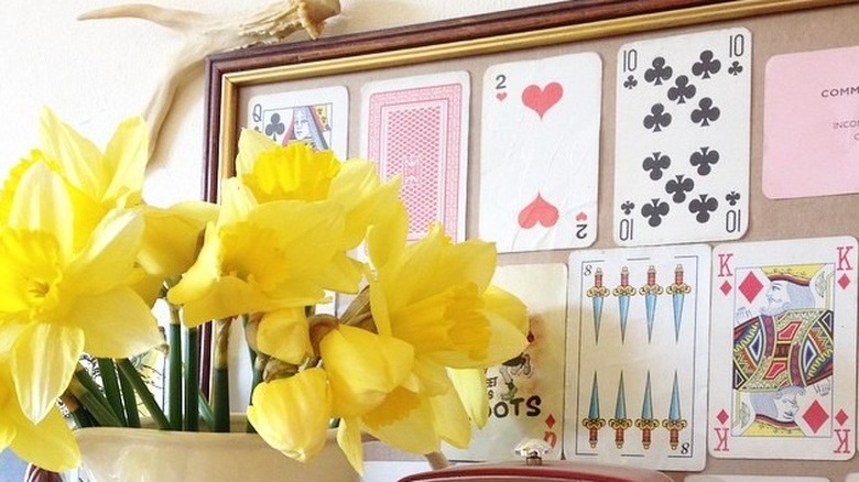 Framed playing cards in the background with a pitcher of flowers in the front