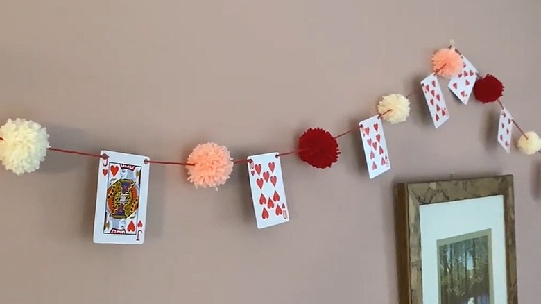 Garland made of playing cards and yarn pompoms hanging on a wall