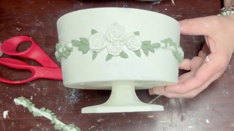 Hand holding an off-white painted trifle bowl with raised, sculpted roses around the bowl