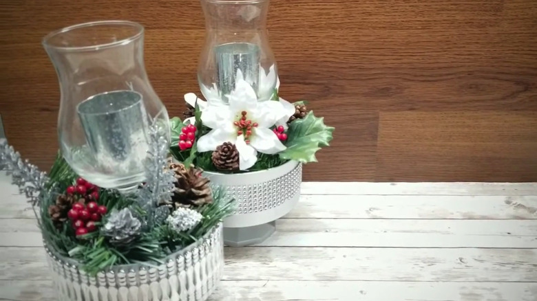 two silver holiday centerpieces on a wood table made from trifle bowls with winter foliage and candle holders in the center