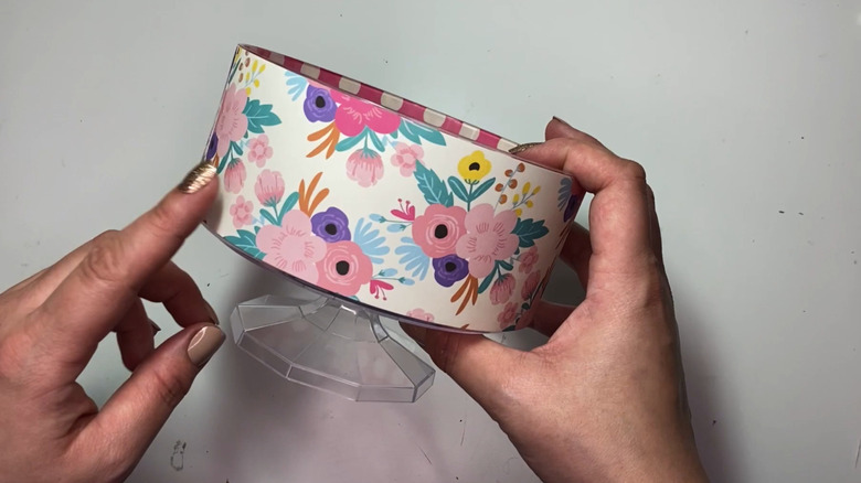 Hands holding a trifle bowl covered in a light, floral designed paper