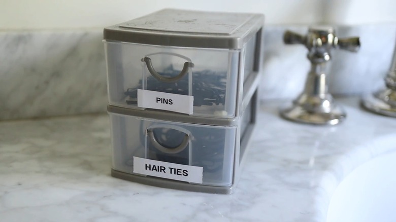 A plastic drawer holding pins and hair ties on a bathroom counter