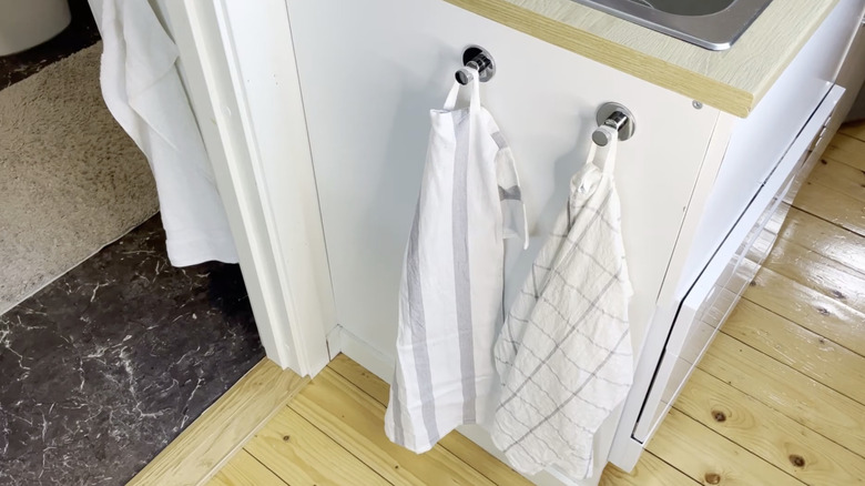 Two kitchen towels hanging from wall-mounted hooks on the side of a kitchen cabinet.
