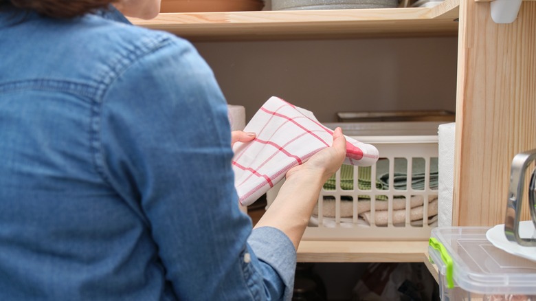 Person holding a white and red check dish cloth by a closet with a white basket.