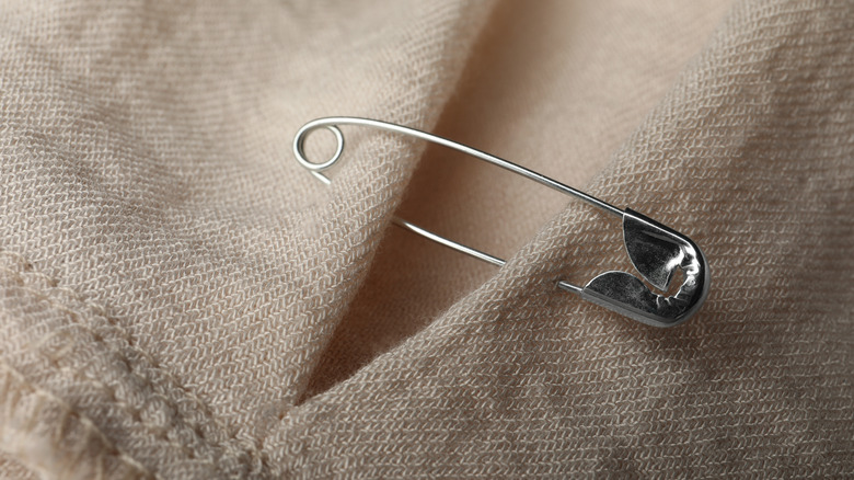 Close-up of a silver safety pin used to join two pieces of tan cloth.