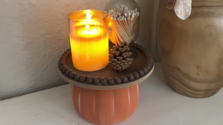 Fall display tray with a plastic pumpkin as the base and a candle, matches, and pinecone on top