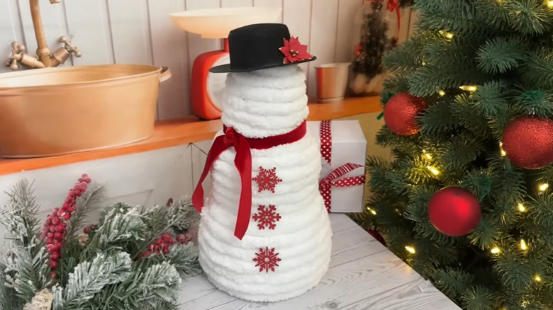 Stacking pumpkins covered in white yard and decorated like a snowman with Christmas decor in the background