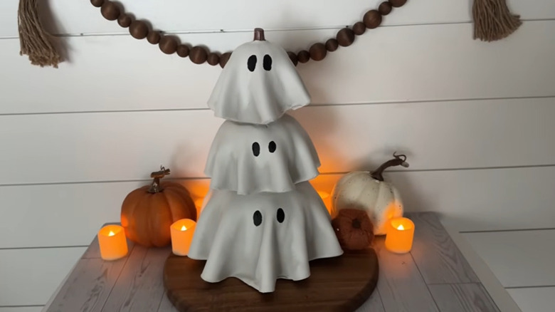 Stack of ghosts made from pumpkins covered in white clay with candles and pumpkins in the background