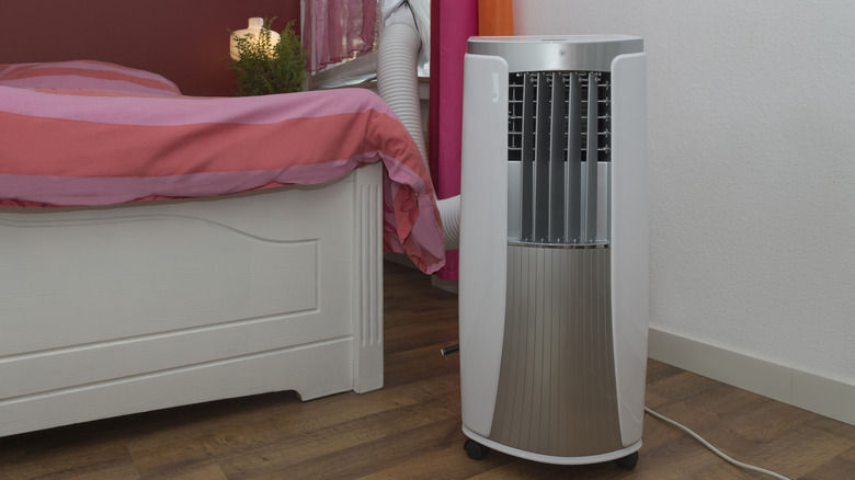 Portable air conditioner sitting next to a white bed
