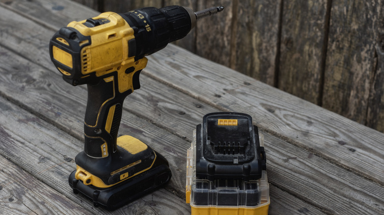 Yellow drill and battery charger sitting on a wooden bench
