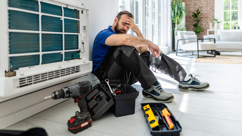 Workman looking worried with a drill and other tools around him