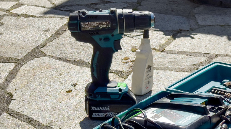 Makita drill with bottle of oil on paving slabs